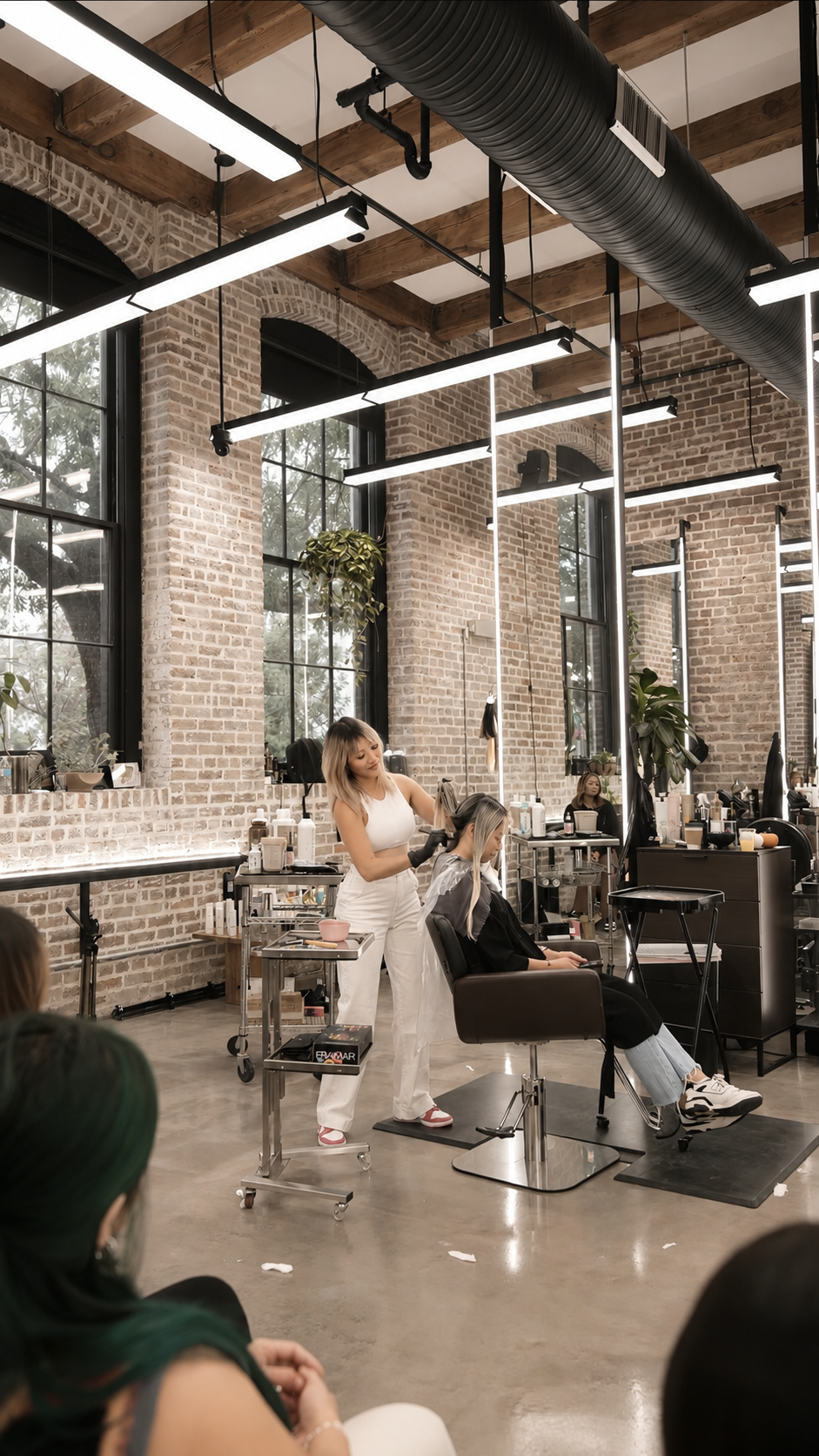 Jennifer Slim working on a guest in a bright brick-walled salon studio during class.